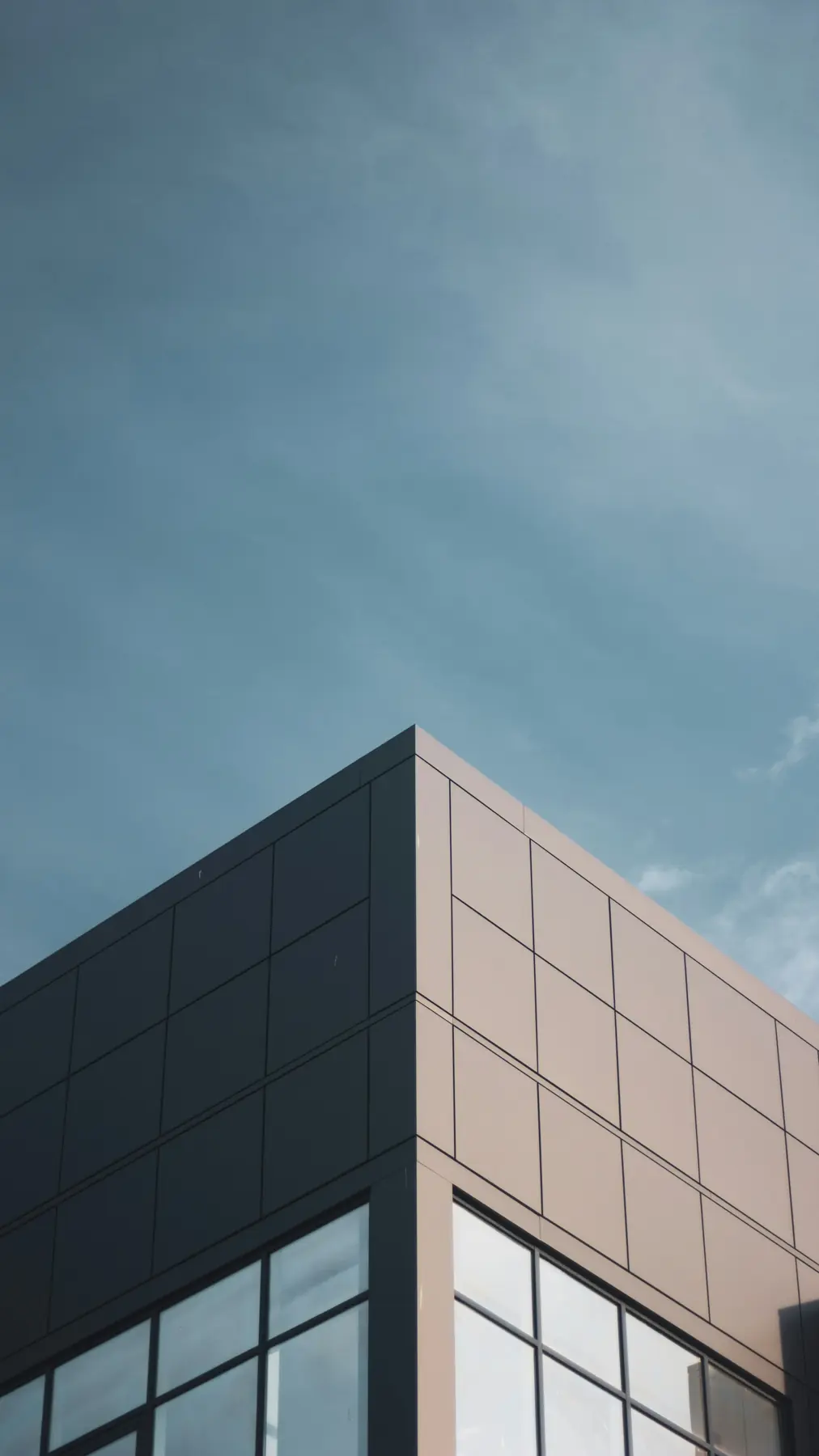 Esquina de edifício comercial com fachada de vidro e painéis metálicos contra o céu