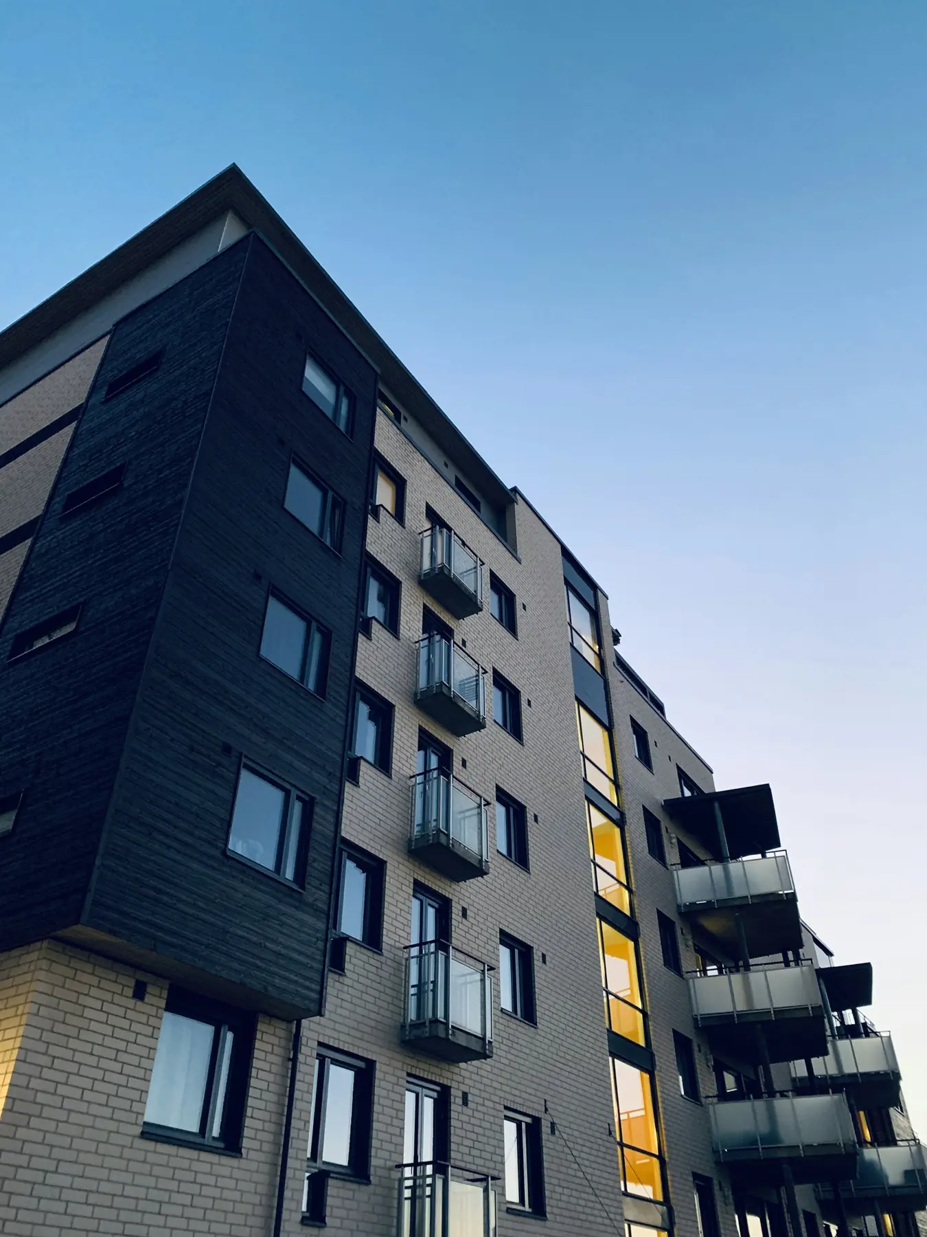 Edifício residencial de fachada escura com varandas, visto de baixo contra o céu azul